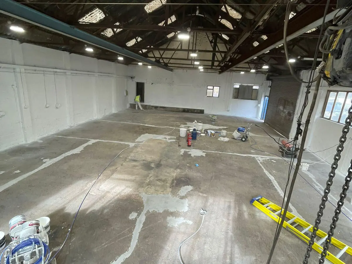 Industrial warehouse mid-project with worker painting white walls and spray equipment on concrete floor