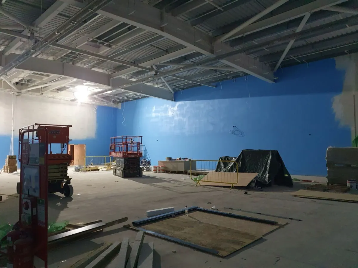Large retail unit interior with bright blue walls freshly painted and scissor lifts on site