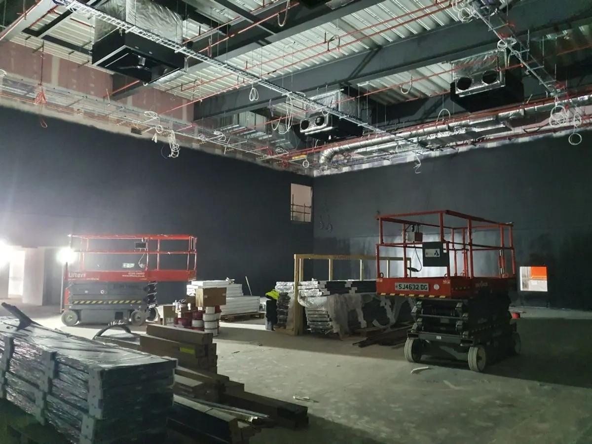 Commercial venue interior painted dark charcoal with scissor lifts and exposed ceiling services