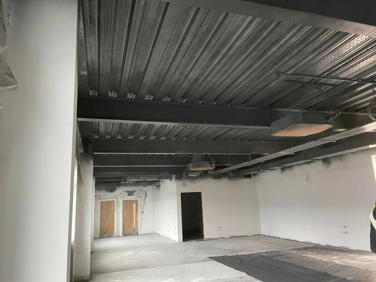 Commercial corridor with freshly painted dark ceiling steelwork and white walls with doors masked off