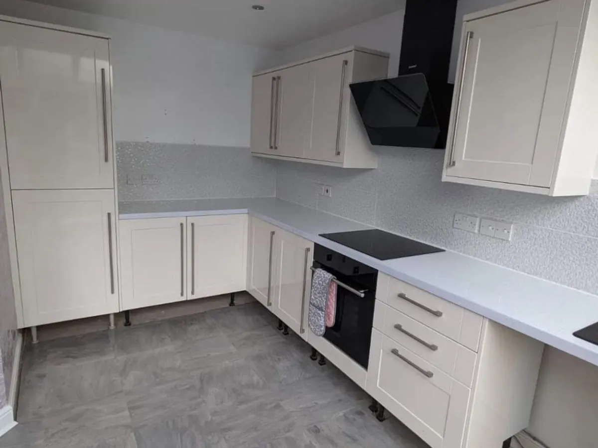 Modern L-shaped kitchen with cream sprayed shaker units black extractor and grey worktops