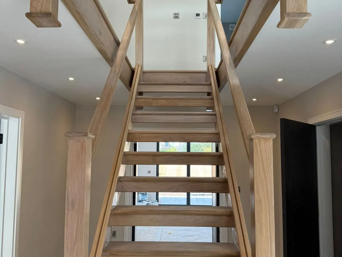 Open-tread oak staircase with glass balustrade in freshly painted hallway with downlights