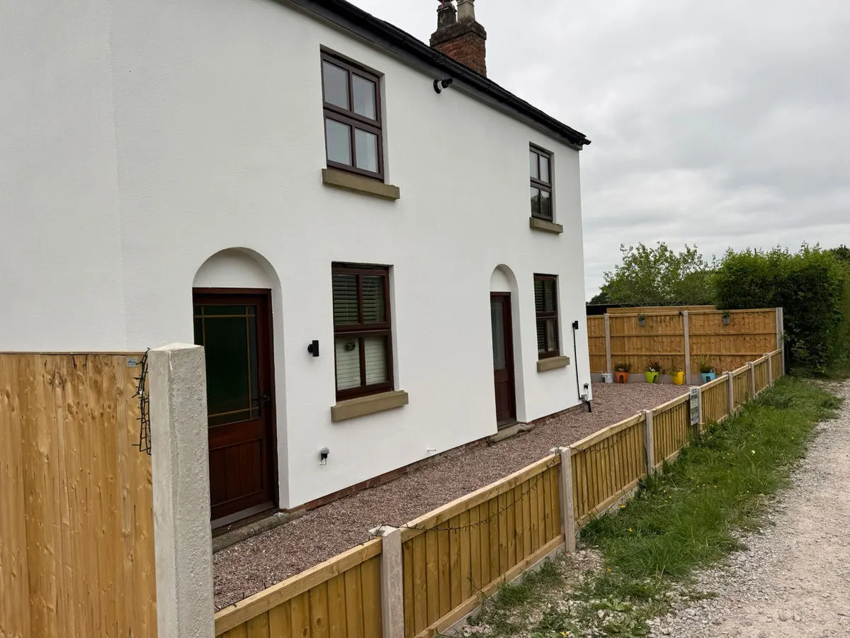Freshly rendered white cottage with dark brown sprayed UPVC windows and new timber fencing